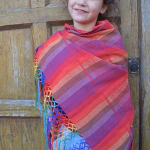 Niña usando la bandolera indajani yee rojo a modo de bufanda apoyada en una puerta