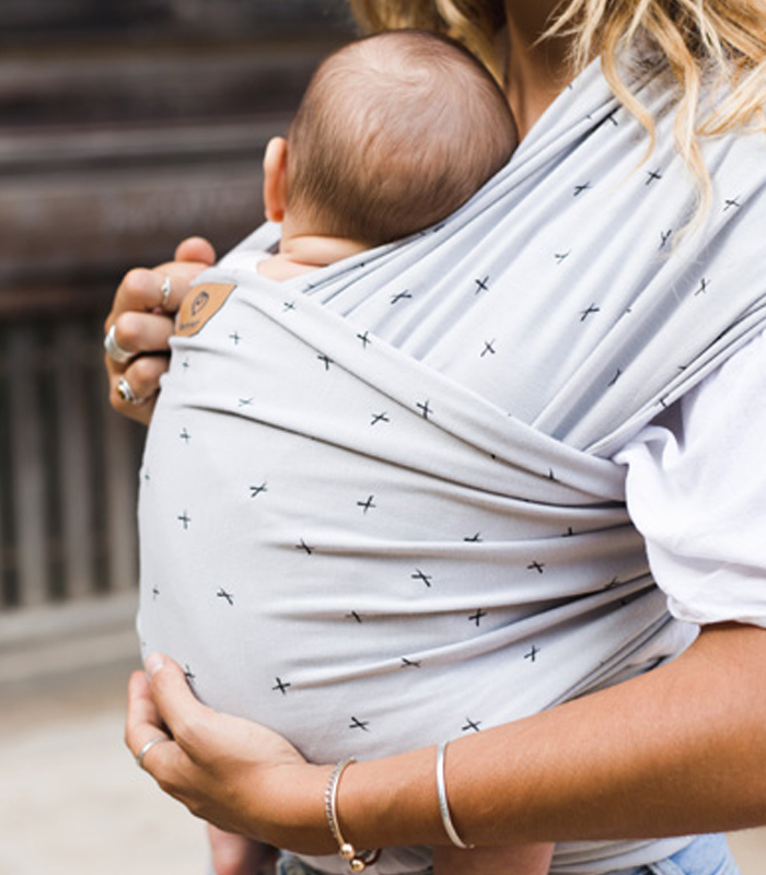Madre abrazando a su bebé recién nacido, que está porteado en un fular elástico de la marca Baby on Earth con un suave estampado de cruces.
