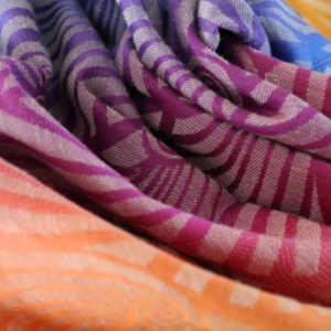 Primer plano de la textura y el patrón geométrico del fular tejido Yaro 'Dandy Habana Grad', mostrando la vibrante transición de colores desde el morado al naranja.