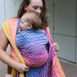 Mujer ajustanto el fular Yaro Dandy Havana Grad, en un parque mostrando el degradado de colores desde el morado al naranja.
