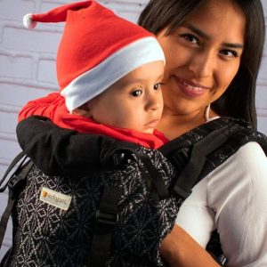 Mujer porteando cómodamente en una mochila negra y plata indajani a su bebé en un parque