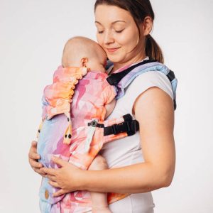 Madre de lado sobre fondo blanco porteando a su bebé en una mochila ergonómica y evolutiva Lenny Lamb, modelo UpGrade, con el colorido diseño Swallows Rainbow Light.