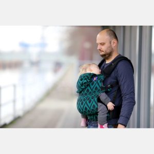 fotografía de un padre porteando a su bebé porteado en una mochila ergonómica Yaro Flex, con el diseño de hojas 'La Vita' en colores negro y verde esmeralda