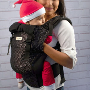 Mujer porteando cómodamente en una mochila negra y plata indajani a su bebé en un parque