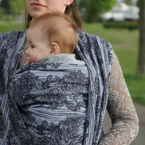 Madre porteando a su bebé al aire libre con el fular tejido Yaro Jazz Duo Black, con un diseño de flores en blanco y negro.