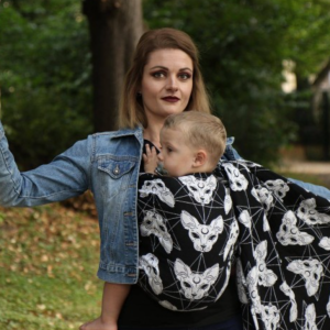 foto de frente Madre porteando a su hijo en la cadera con el fular tejido Yaro Sphynx Trinity, en blanco y negro con estampado de gatos esfinge y lunas