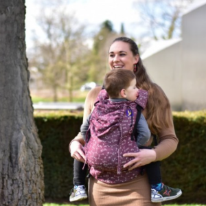 Madre porteando a su hijo en el pecho con la mochila ergonómica Yaro Hug Chemic Chianti, de color vino con un estampado de fórmulas químicas y diagramas moleculares en blanco.
