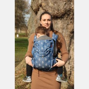 Madre sonriente porteando a su hijo toddler al aire libre con la mochila Yaro Hug Sailor Blue, de color azul marino con estampado de anclas blancas
