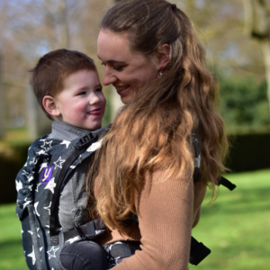 Madre jugando con su hijo mientras lo portea en la mochila ergonómica Yaro Hug Stellar Black, con un diseño de estrellas blancas dibujadas sobre fondo negro.