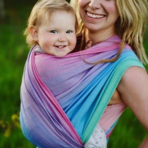 Primer plano de madre y bebé sonriendo felices, envueltos en el fular tejido Little Frog Lolite con mezcla de Tencel, mostrando los suaves tonos rosa, azul y morado.