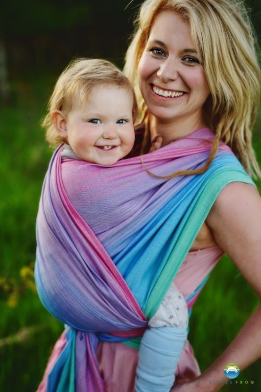 Primer plano de madre y bebé sonriendo felices, envueltos en el fular tejido Little Frog Lolite con mezcla de Tencel, mostrando los suaves tonos rosa, azul y morado.