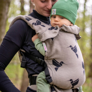 Madre porteando a su bebé foto de lado en un bosque con la mochila ergonómica MoniLu Uni Start, de color arena con estampado de colibríes negros