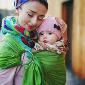 Madre porteando a su bebé con una bandolera de anillas Little Frog modelo Olivine, de color verde brillante con rayas sutiles y cola larga.