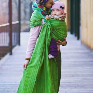 Madre caminando al aire libre porteando a su bebé en la cadera con una bandolera verde Little Frog, mostrando la libertad de movimiento.