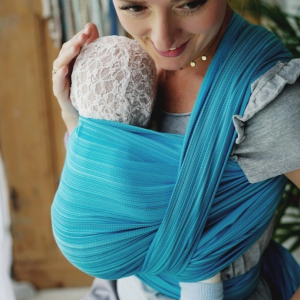 Madre sonriendo con fular tejido de rayas azules, mostrando cómo el gramaje ligero de 220 g/m² permite un nudo pequeño y cómodo en la cintura.
