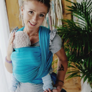 Madre porteando a su bebé al frente con un fular tejido Little Frog Aquamarine talla 6, mostrando el color azul turquesa vibrante.