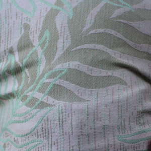 Primer plano de una mano sujetando la tela del fular Oasis, mostrando la textura del tejido Jacquard y el relieve del patrón de hojas.