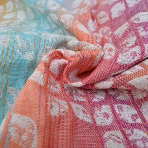 Detalle macro del tejido formando un remolino, donde el patrón de pétalos blancos resalta sobre la mezcla de fibras de colores vibrantes.