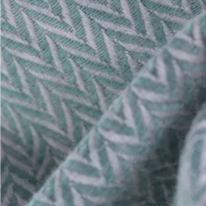 Primer plano del tejido de fular de la mochila Buzzidil, mostrando el patrón en espiga (herringbone) que entrelaza hilos color jade y blanco.