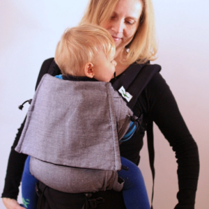 Madre porteando a su hijo mayor a la espalda con la mochila Buzzidil Sherlock, mostrando cómo el panel evolutivo cubre perfectamente la espalda del niño.