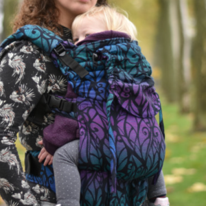 Madre porteando con la mochila Yaro Hug confeccionada con tejido Solnce Genesis Hummingbird en tonos morados y azules.