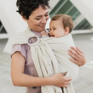 Madre con pelo corto sonriendo a su bebé porteado en la bandolera de anillas Boba Ring Sling en lino y bambú color Pampas Beige.