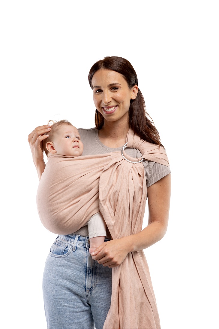Fotografía de catálogo con fondo blanco de madre sonriendo con su bebé ergonómicamente alojado en la bandolera de anillas Boba Ring Sling color Peony Pink.