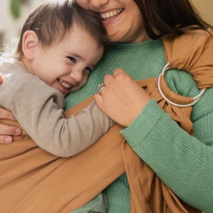 Madre e hijo mayor riendo juntos mientras el niño va porteado a la cadera en la bandolera de anillas Boba Ring Sling color marrón Rye Brown.