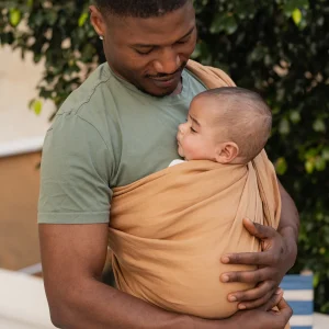 Padre en camiseta verde mirando con amor a su bebé recién nacido dormido sobre su pecho en la bandolera de anillas Boba Ring Sling Rye Brown.
