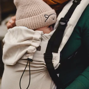 Plano detalle de bebé con gorro de lana protegido en la mochila ergonómica evolutiva Little Frog Prime V3 en color beige Moonstone.