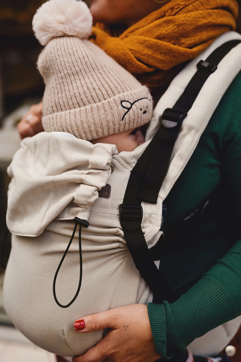 Plano detalle de bebé con gorro de lana protegido en la mochila ergonómica evolutiva Little Frog Prime V3 en color beige Moonstone.
