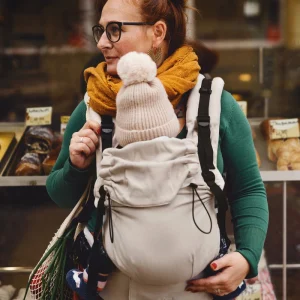 Plano medio de madre mirando al frente con su bebé porteado ergonómicamente en la mochila evolutiva Little Frog Prime V3 color beige.