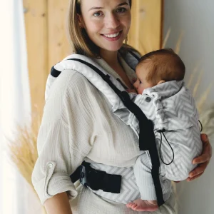Madre de perfil sonriendo mientras sostiene suavemente a su bebé acomodado en la mochila evolutiva Little Frog Prime V3 Platinum Miles.
