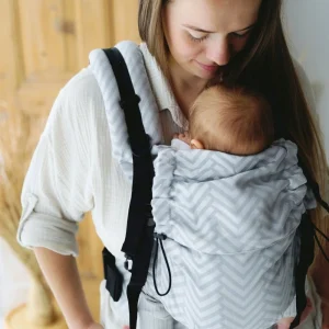 Plano medio de madre mirando con ternura a su recién nacido alojado en la mochila evolutiva gris y blanca Little Frog Prime Platinum Miles.