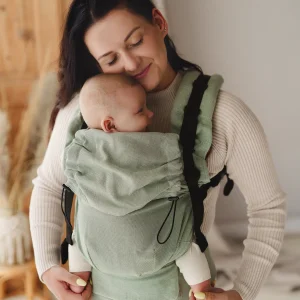 Madre con los ojos cerrados sosteniendo a su bebé en la mochila ergonómica evolutiva Little Frog Prime V3 en tejido de fular verde salvia Sage Moonstone.