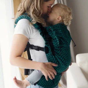 Madre de perfil rozando suavemente su nariz con la de su bebé sonriente porteado en la mochila evolutiva Little Frog Prime Viridian Miles.