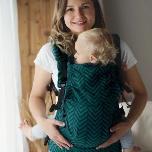 Plano medio de madre sonriendo a cámara con su bebé acomodado ergonómicamente en la mochila evolutiva verde Little Frog Prime Viridian Miles.
