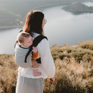 Madre porteando a su bebé a la espalda con la mochila Néobulle My Néo Grey contemplando un paisaje natural con lago.