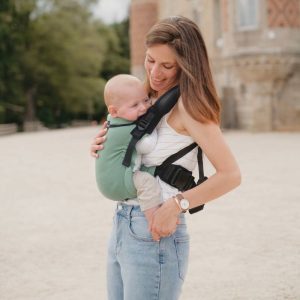 Madre sonriendo mientras sostiene a su bebé ergonómicamente alojado al frente en la mochila evolutiva Néobulle My Néo en color verde menta.
